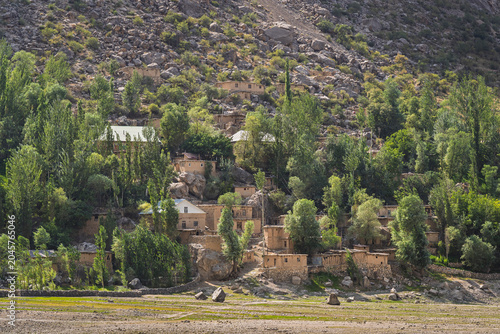 Scenic landscape view of traditional rural village among trees on the shores of Marguzor lake in late afternoon, Haft Kul, Sughd, Tajikistan