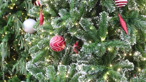 big christmas tree with fake snow and red swirl ornaments. bright warm lights shining on green branches. traditional holiday setup