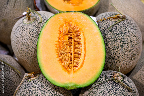 Close up of a cantaloupe melon cut in half revealing juicy orange flesh and seeds with a background of whole netted melons