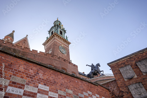 Historic castle wall with clock tower and statue seen during sunny day in Krakow, Poland