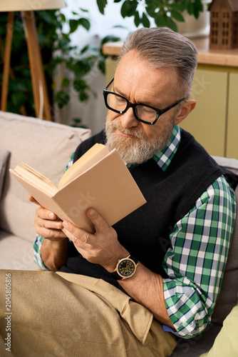 Senior man with beard enjoying a quiet afternoon reading in a modern apartment