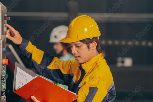 Schilderij op canvas Group of diverse Asian technicians and female industry specialists collaborating next to production machinery, checking maintenance checklists and auditing plant operations to ensure workplace safety