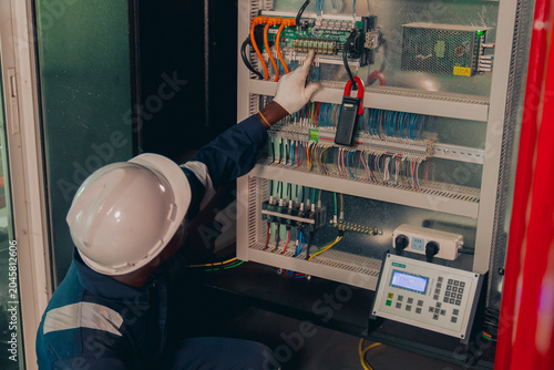 Black male maintenance specialist in safety gear tracking logistics data or automation software on a tablet screen during factory operation, showcasing digital transformation and workforce diversity.