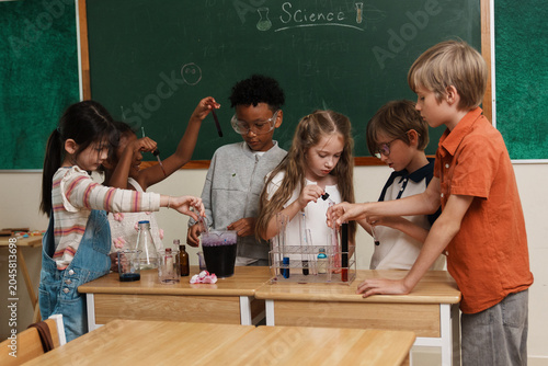 A group of multi-ethnic school children pouring liquids and mixing colorful chemicals in test tubes, enjoying a hands-on STEM education class and interactive teamwork activity.