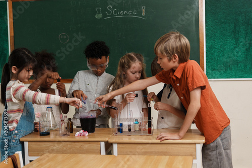 A group of multi-ethnic school children pouring liquids and mixing colorful chemicals in test tubes, enjoying a hands-on STEM education class and interactive teamwork activity.