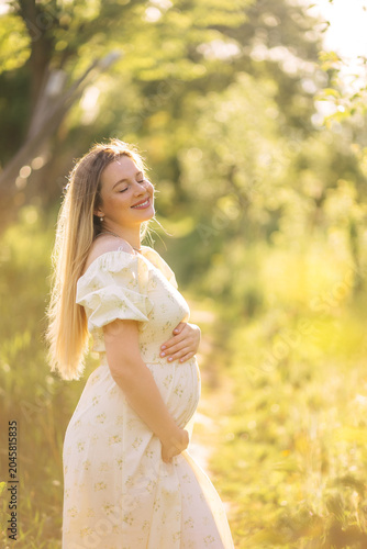Pregnant woman in a floral maternity dress enjoying golden hour sunlight in a peaceful summer meadow