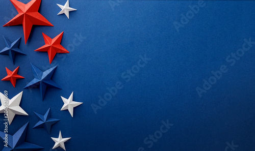 Festive arrangement of red, white and blue paper stars and curled ribbons on dark blue background. Patriotic border with empty space for text, suitable for Independence, Fourth of July, Memorial