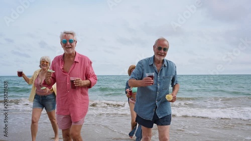 Happy senior friends dancing and drinking on the beach