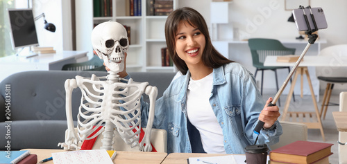 Female student with human skeleton model taking selfie at university