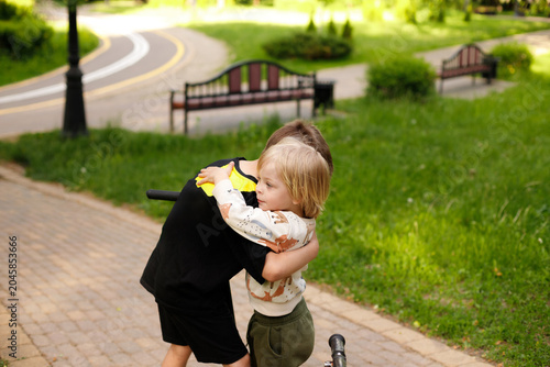 Canvas Print Two happy brothers boys hugging and embracing after falling from kick scooters o