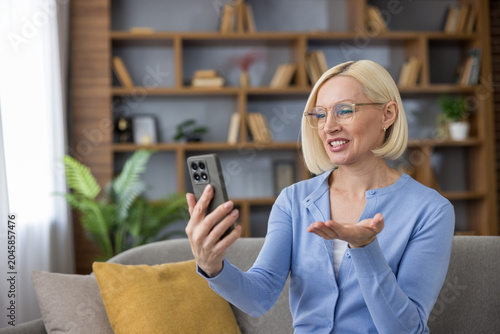 Принти на полотні Blonde woman with glasses smiling and gesturing during a smartphone video call f
