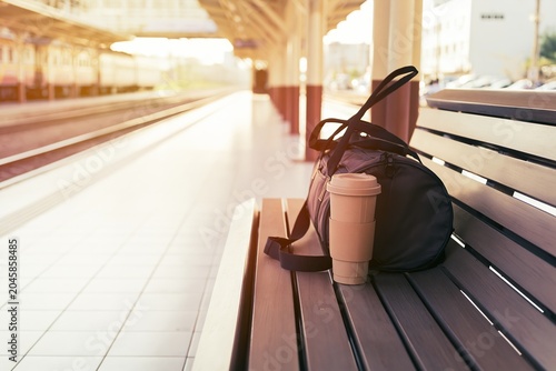Coffee tumbler and travel bag on train platform bench