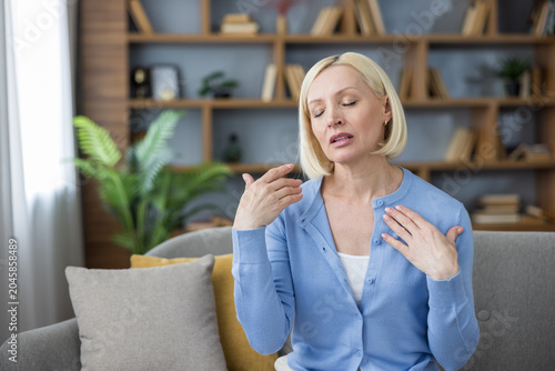 Cuadro en lienzo Blonde middle-aged woman on a sofa fanning herself during a sudden hot flash at
