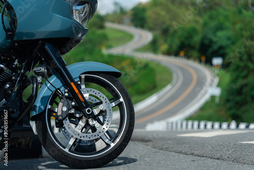 Sleek motorcycle with shiny chrome wheels is parked on winding road, surrounded by lush greenery, evoking sense of adventure