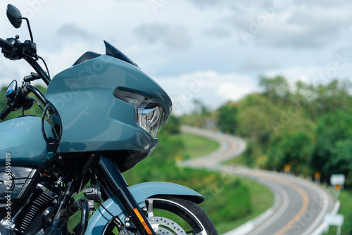 Sleek motorcycle with modern design is parked on winding road, surrounded by lush greenery and cloudy sky