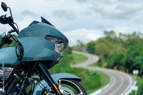 Sleek blue motorcycle parked on scenic winding road, surrounded by lush greenery and cloudy sky