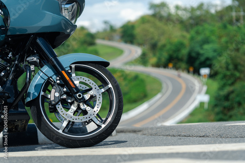 Sleek motorcycle with shiny chrome wheels is parked on scenic winding road, surrounded by lush greenery and clear sky