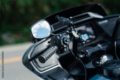 Close up of motorcycle handlebar with mirror and control buttons, showcasing modern design and technology