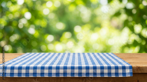 Picnic blanket layout pattern over wooden table outdoors with nature background bokeh light. summer leisure park. background fabric display, material textile nature, simple design surface