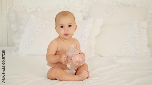 an infant drinking water or milk from a bottle or cup, a young child eating or sucking water on a bed at home, the concept of baby food