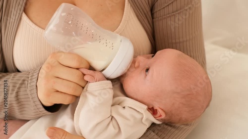 baby sucks on a bottle of milk, mother feeds newborn baby from a bottle of milk at home, mother holds a small baby and feeds it with milk