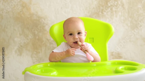 baby with a feeding spoon, little child eating in a high chair waiting for food, first solid food, baby food concept