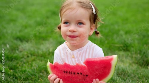a child eating a watermelon in a park, a baby on a green lawn in summer with a watermelon