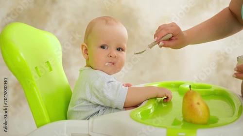 feeding a baby, mother feeding a baby boy with a spoonful of fruit puree in a green high chair, baby food