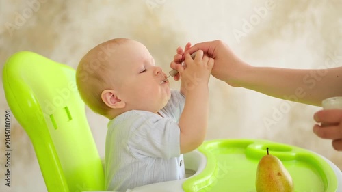 feeding a baby, mother feeding a baby boy with a spoonful of fruit puree in a green high chair, baby food