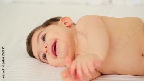 baby in diapers on a white bed at home, space for text, little child boy smiling on the bed before bedtime in diapers