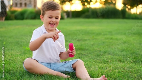 a little boy with bubbles is playing on a green lawn in the summer, having fun, a child is walking in the summer evening laughing and smiling, summer holidays