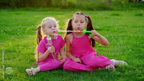children blowing bubbles in the park in summer, two girls walking and having fun on a green lawn, summer holidays