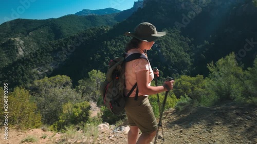 Woman hiking on mountain trail with backpack and trekking pole overlooking forest valley