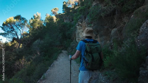 Hiker with backpack and hat walking on a rocky forest trail