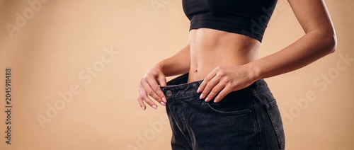 Healthy weight loss result concept with a slim woman showing a wide waist gap in large black jeans