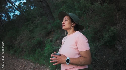 Woman in hat holding a camping mug while pausing on a forest hike at dusk
