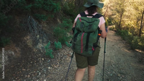 Woman hiking on a forest trail with large backpack and trekking poles at golden hour