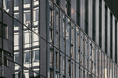 A mirrored glass facade shows reflection and shadow across office windows, where urban grid lines deepen the building surface in layered geometry