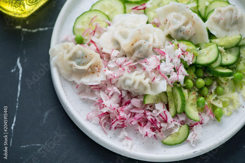 Panasian salad with vegetables and wontons on a white plate, horizontal shot on a black marble surface, closeup