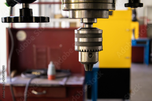 Close-up of a metal drill chuck on an industrial vertical drilling machine