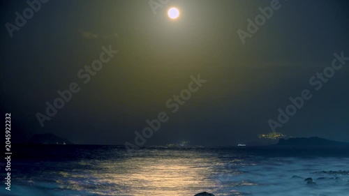 A bright full moon rises over the dark ocean at night in Shimen, New Taipei, Taiwan, with moonlight reflecting on the water surface.
