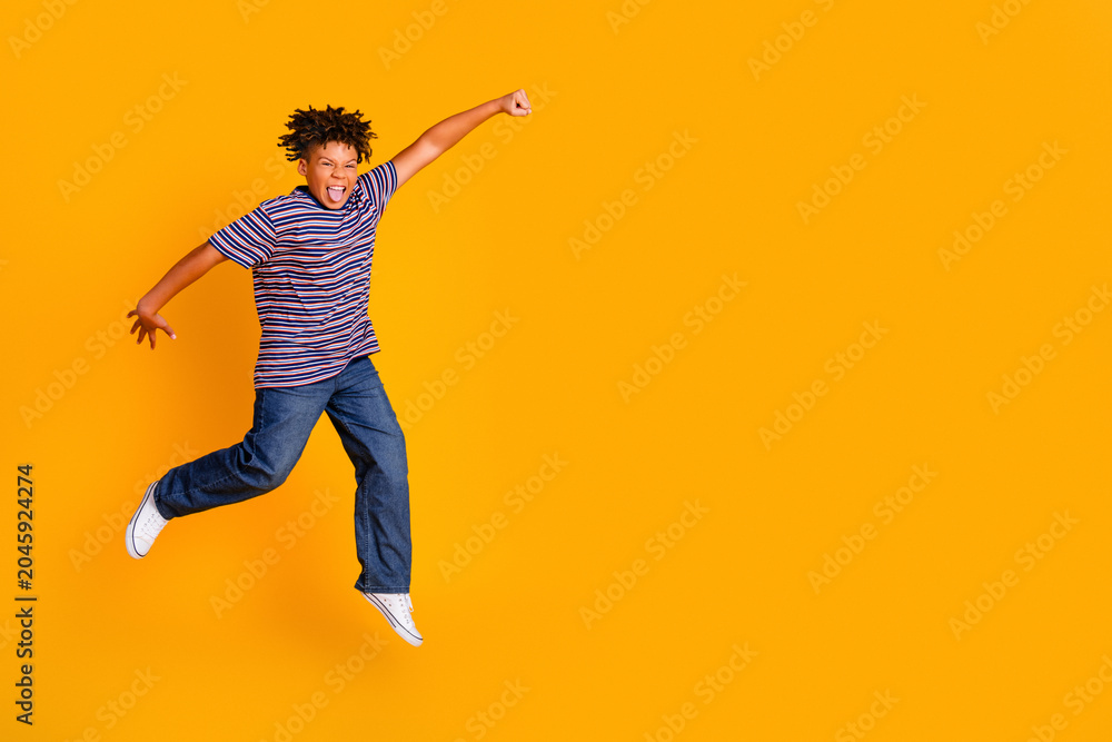 Naklejka premium Joyful boy jumping in striped t-shirt and jeans on bright orange background, energetic playful childhood moment with an expressive smile
