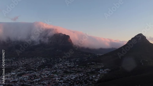 Aerial drone footage of low clouds rolling over Table Mountain with Lion’s Head emerging into frame above Cape Town, South Africa.