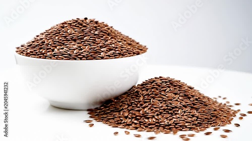 Pile of brown flax seeds with white bowl.