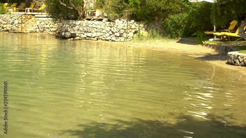 Crystal clear water near the sandy shore. The sandy bottom is visible through the water. Sun glare plays on small waves. A quiet summer day at a tropical resort.
