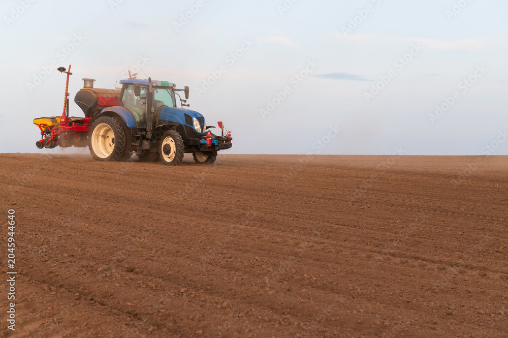 Fototapeta premium Tractor plowing and sowing on agricultural field in spring
