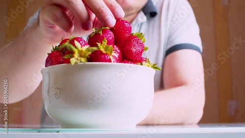 Low angle close-up of man's hands eating ripe strawberries from a bowl, blurred silhouette background. Shallow depth of field, natural window light.Healthy nutrition -organic food. 