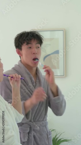 Vertical video: Picking up brushes couple brushing teeth at bathroom sink in robes headband morning