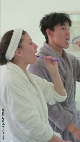 Vertical video: Reaching for toothbrushes, couple in robes brushing teeth at sink in morning