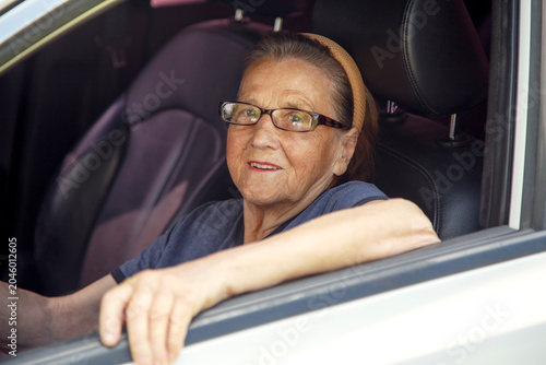 Old woman driving a car in the countryside, road trip concept.  Portrait of an old woman driving and near a car, on a walk outside the city.
